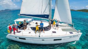 A diverse group joyfully sails a large white catamaran named "SEA ROVER" on clear turquoise Caribbean waters under bright sun.