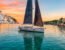 A sleek yacht sails across turquoise waters at sunset, flanked by a Greek village on the left and a Croatian town on the right.